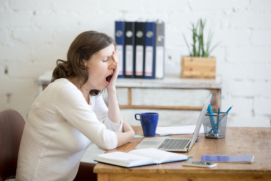 young woman sleep-deprived, sitting at table in front of laptop, sleepy, tired, overworked