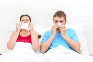 young married couple ill in bed and blows her nose