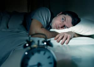 insomnia guy who cant sleep on bed in front of alarm clock