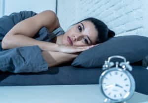 woman lying in bed looking at clock unable to sleep