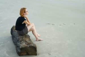 a woman sitting on a log on a beach