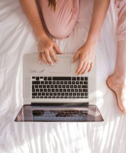 image of person sitting on bed in pink pants shopping on a laptop