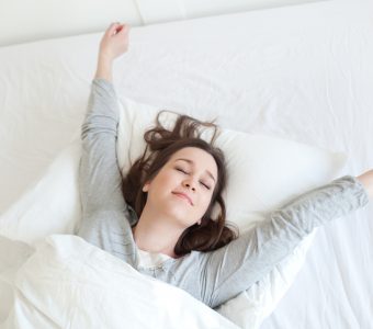 Young woman waking up fully rested on comfortable mattress.
