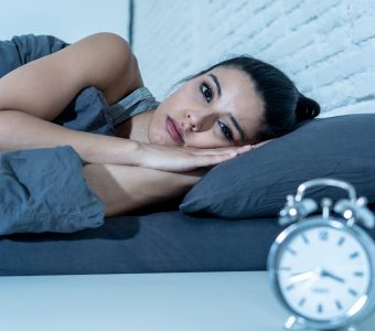 woman lying in bed looking at clock unable to sleep