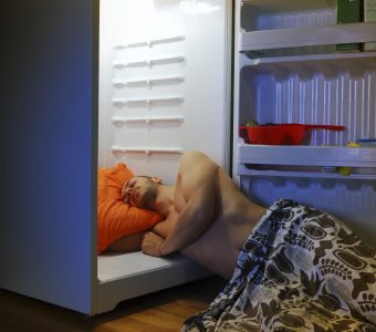 man laying on floor paritally in fridge to cool down