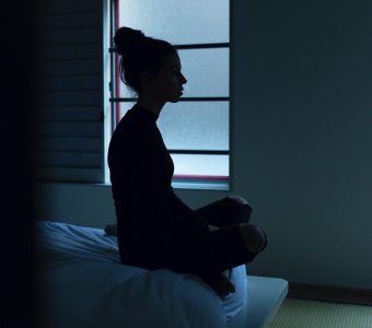 image of woman sitting up in bed at night unable to sleep in the dark next to window